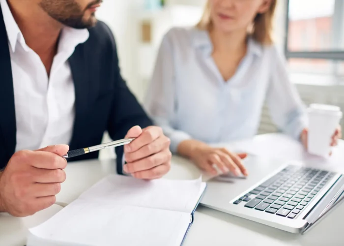 Hands of businessman with pen over open notebook during interaction with colleague